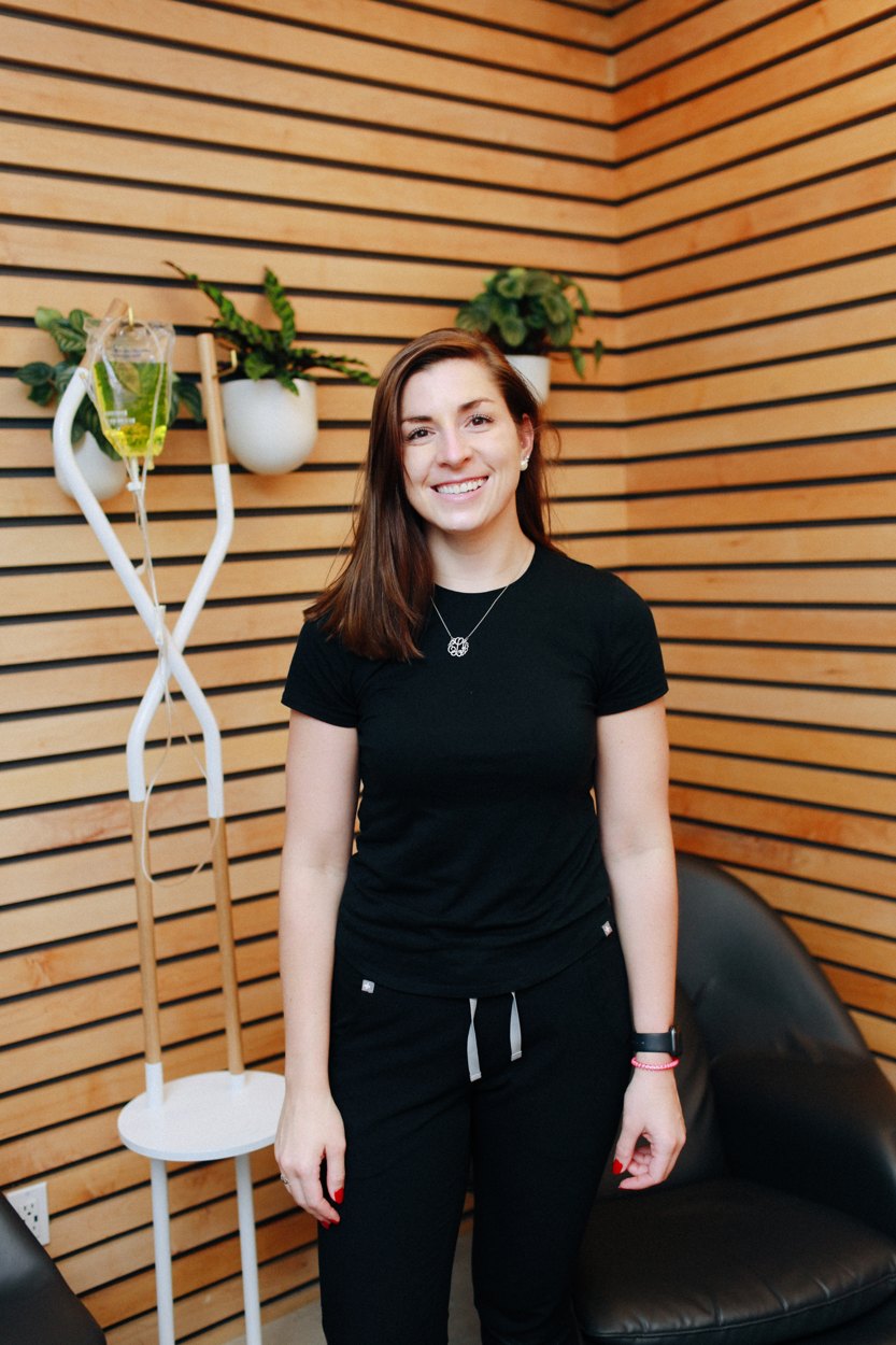 A smiling NutriDrip nurse beside the IV bags in the lounge